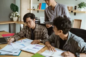 3 mahasiswa sedang berdiskusi sambil melihat data